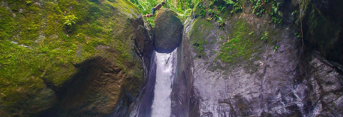 man standing on balanced rock of pavon waterfall tour manuel antonio